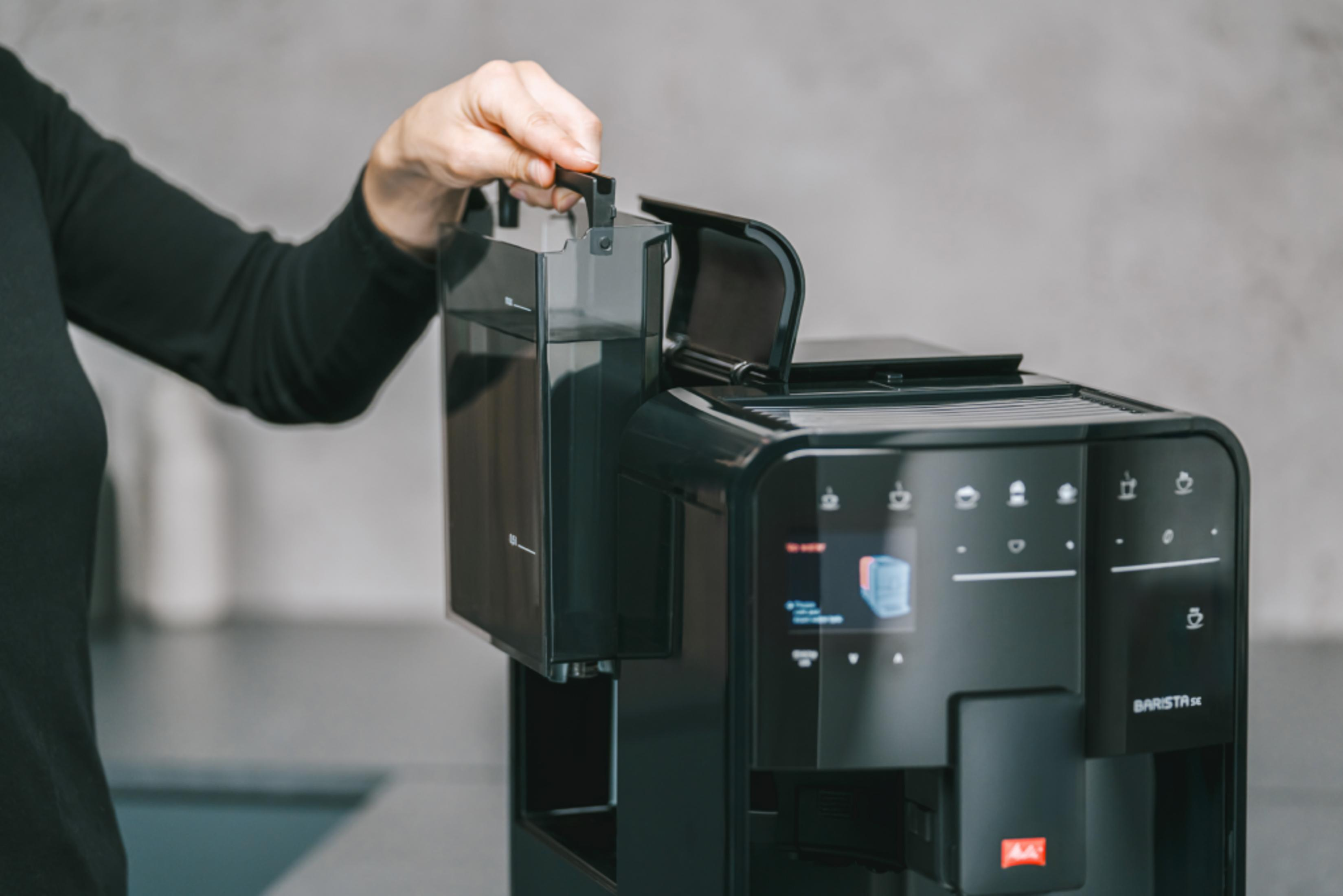 Ręka wyciąga zbiornik na wodę z ekspresu do kawy.