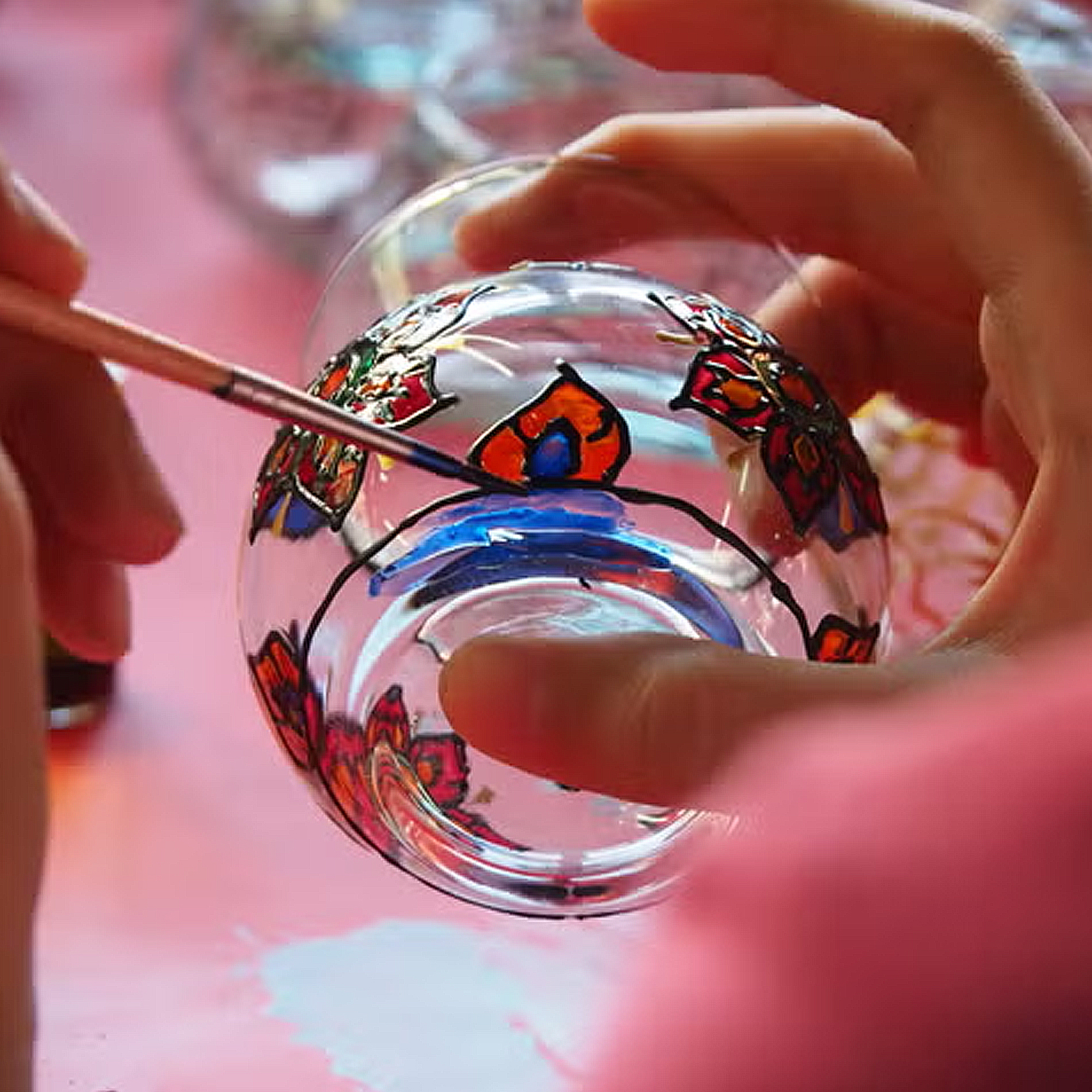 Mani dipingono un bicchiere con un pennello, colori rosso e blu.