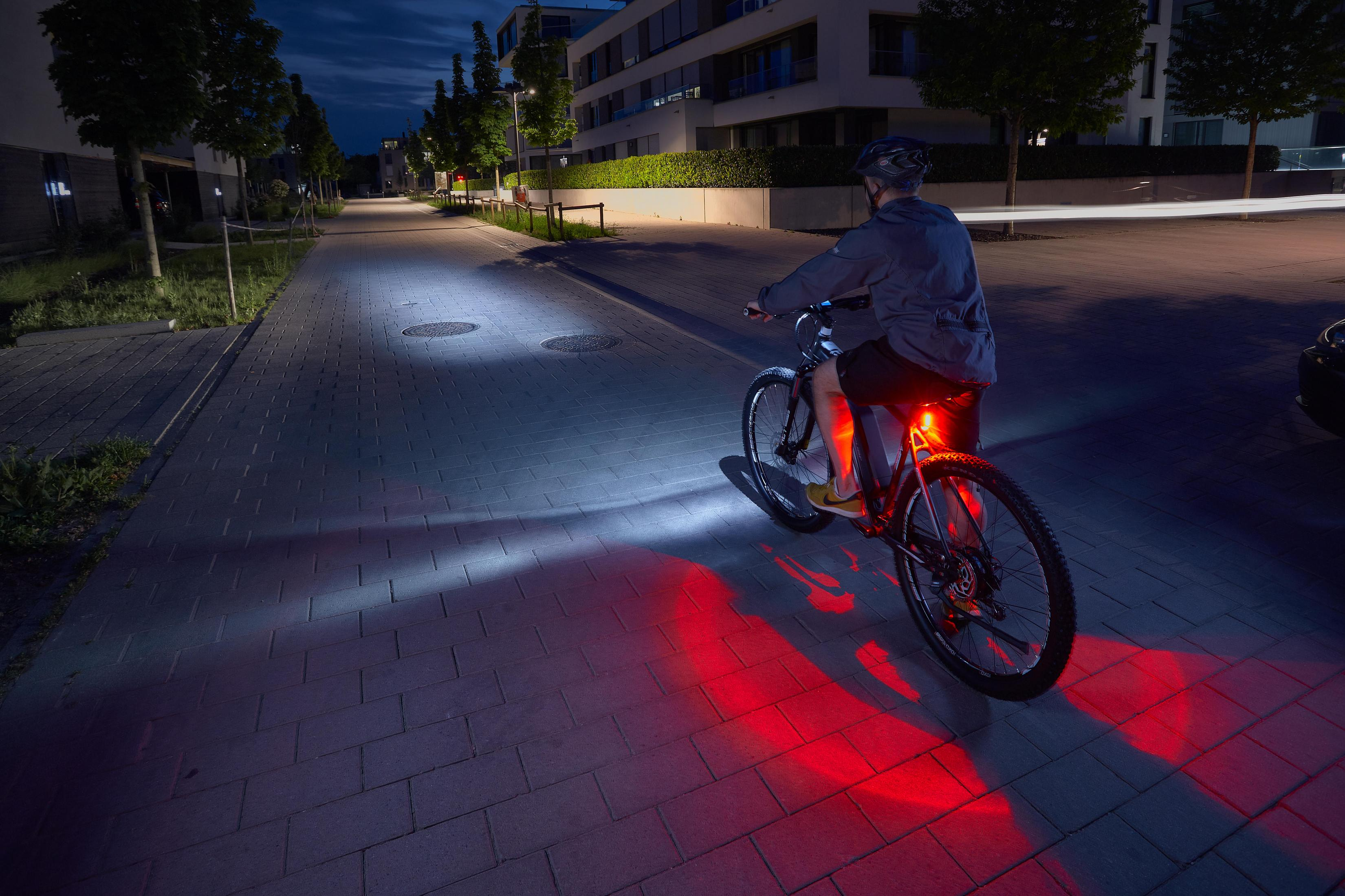 Ein Radfahrer fährt nachts auf einem gepflasterten Weg, beleuchtet von Scheinwerfern und Rücklicht.