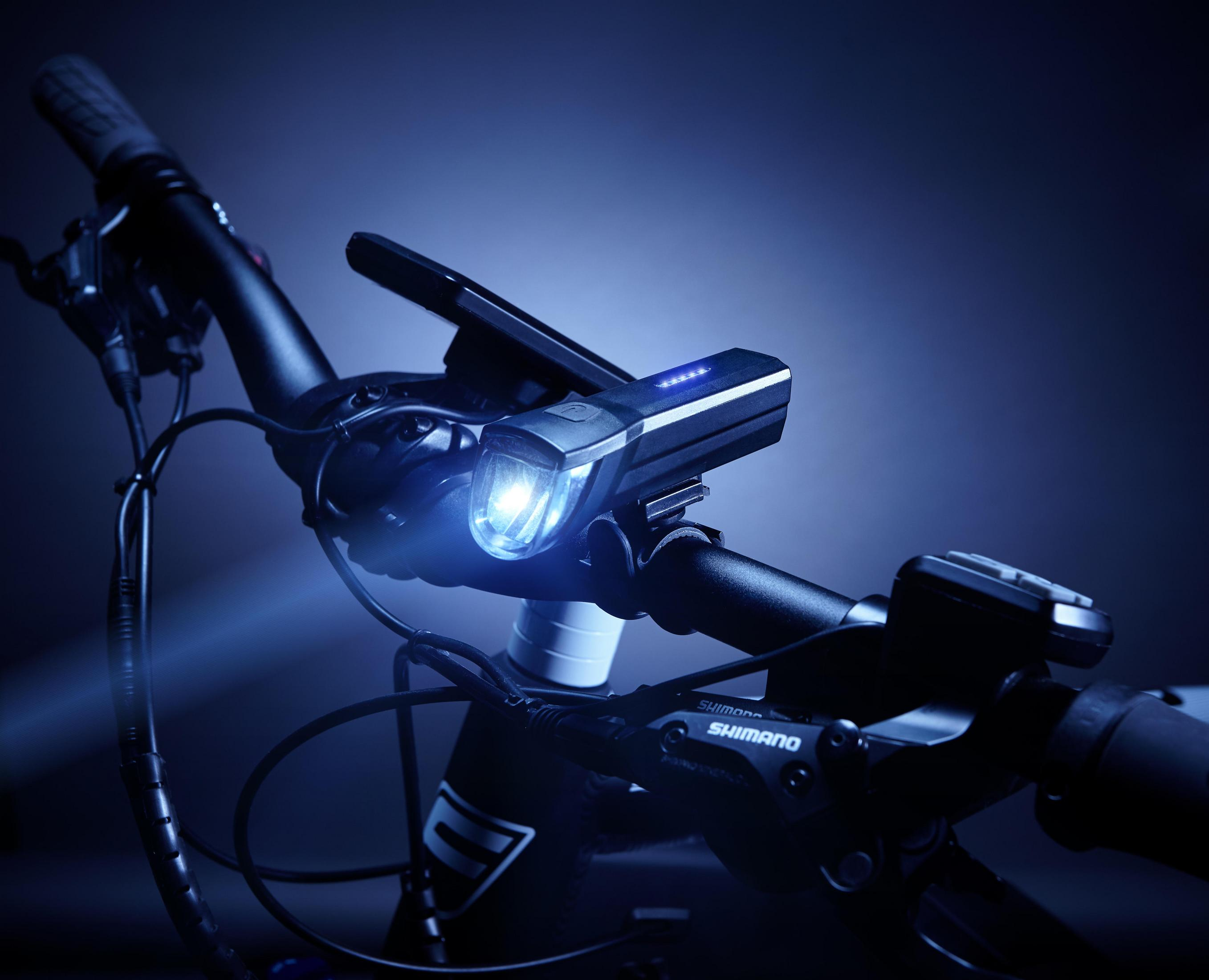 Ein Fahrradlenker mit einem eingeschalteten Vorderlicht und einem Handyhalter.