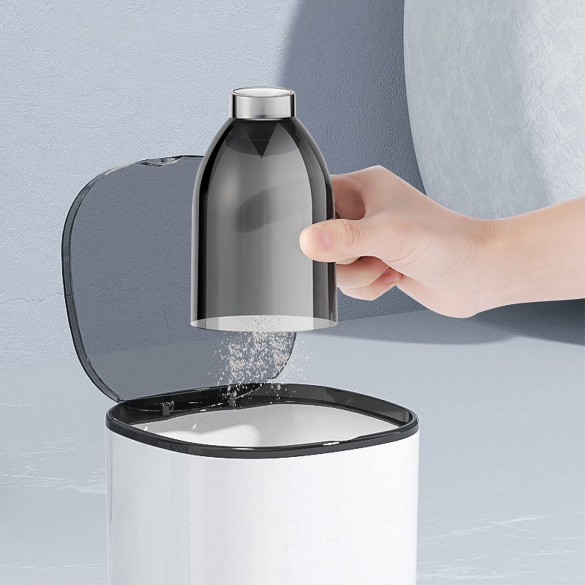 Una mano tiene un contenitore grigio sopra un cestino bianco, con polvere che cade.