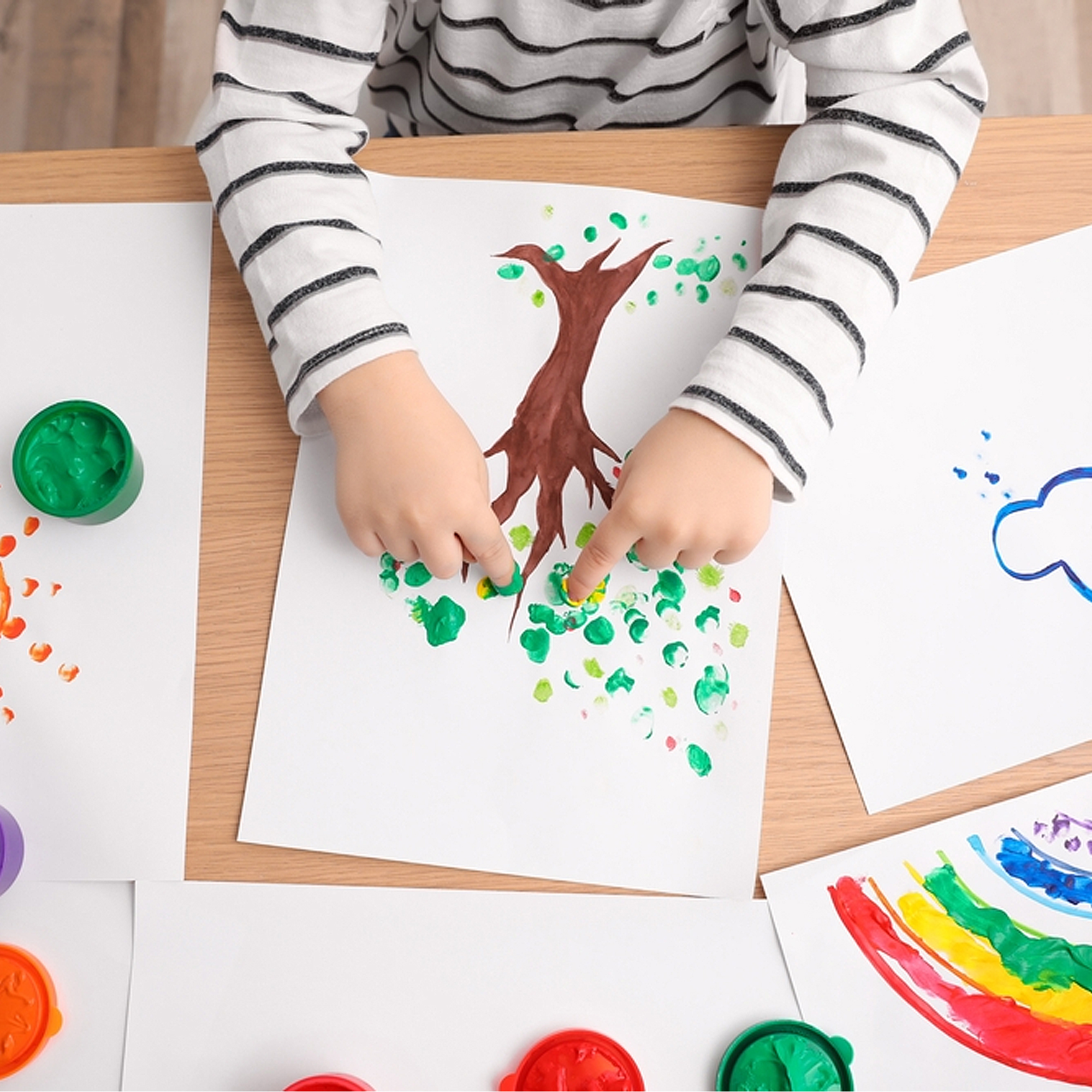 Un bambino dipinge un albero con tempere per dita su carta. Punti verdi decorano l'albero.