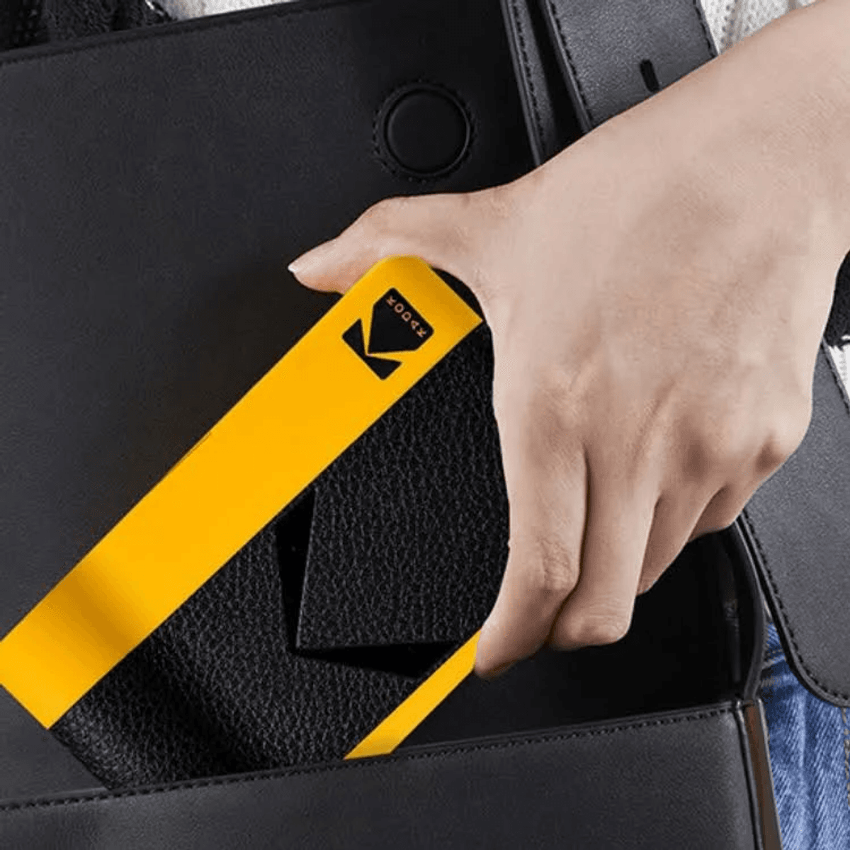 Una mano mete un objeto Kodak amarillo en un bolso negro.