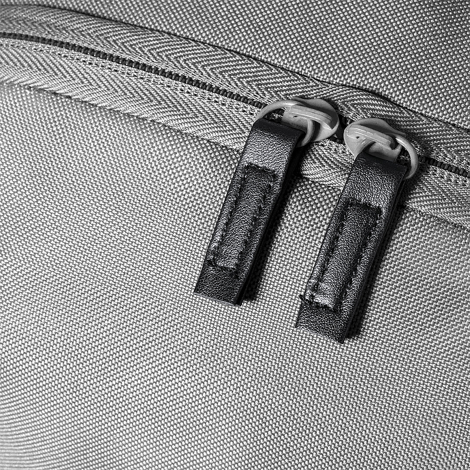 Primo piano di due tiretti con linguette in pelle su una borsa di stoffa grigia.