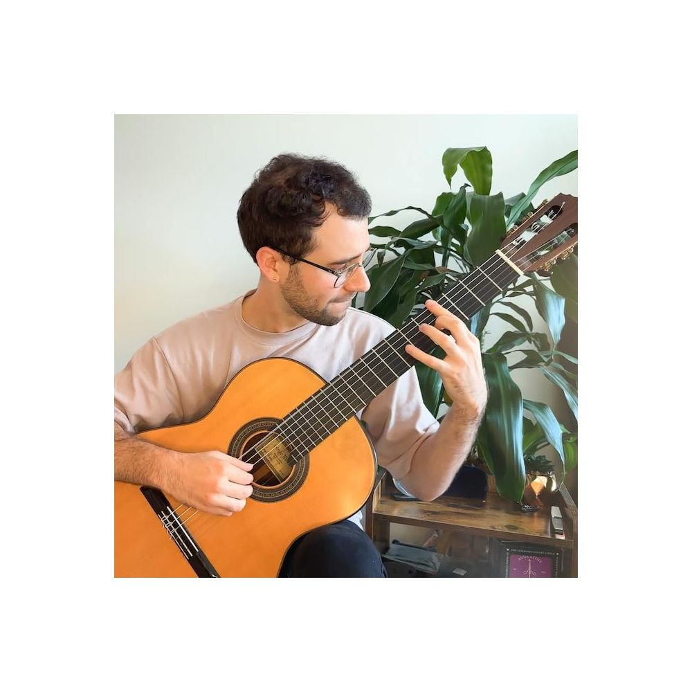 Een man met bril speelt gitaar, met een plant ernaast.