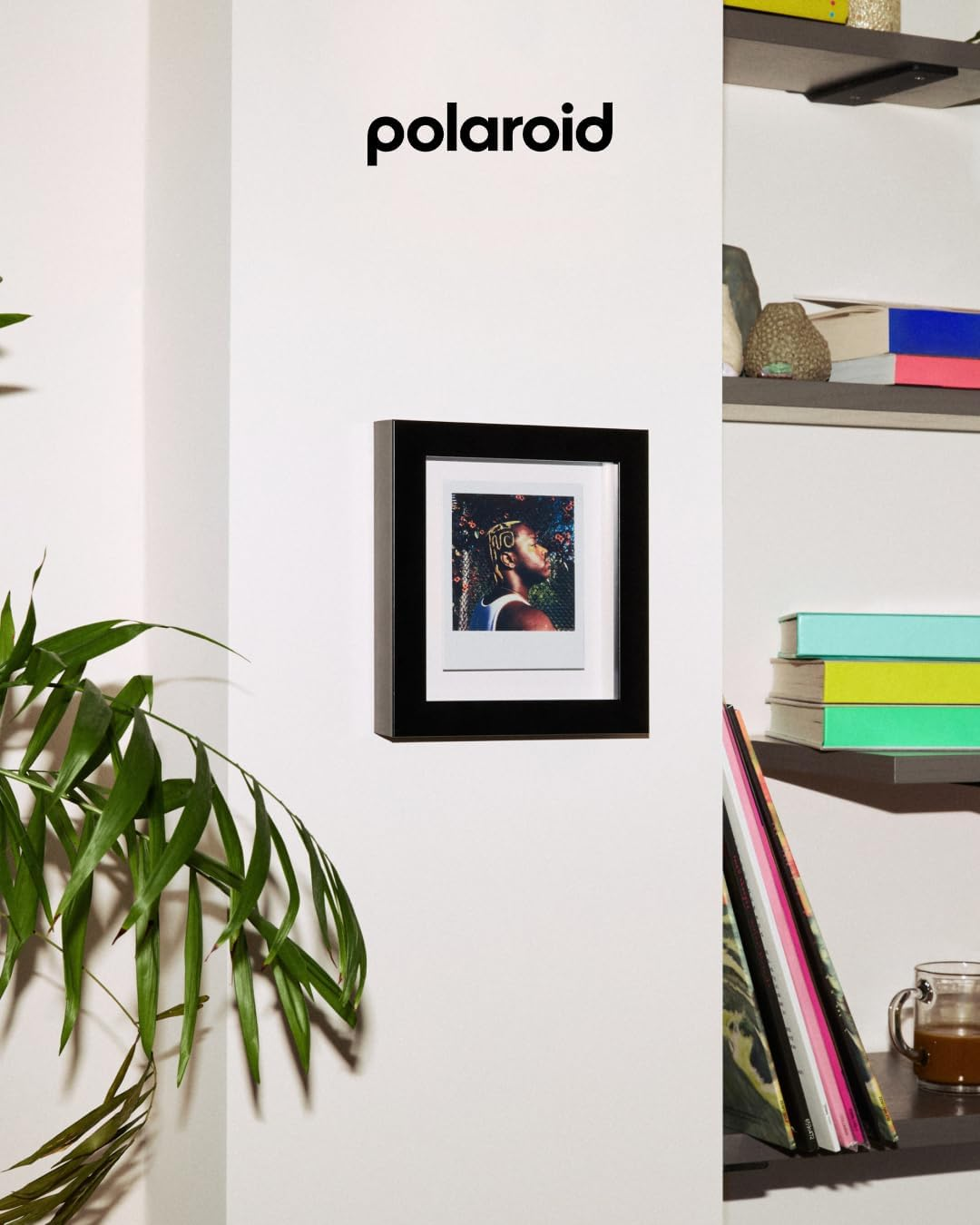 Ein gerahmtes Polaroidfoto einer Person mit Blumen im Hintergrund hängt an der Wand.