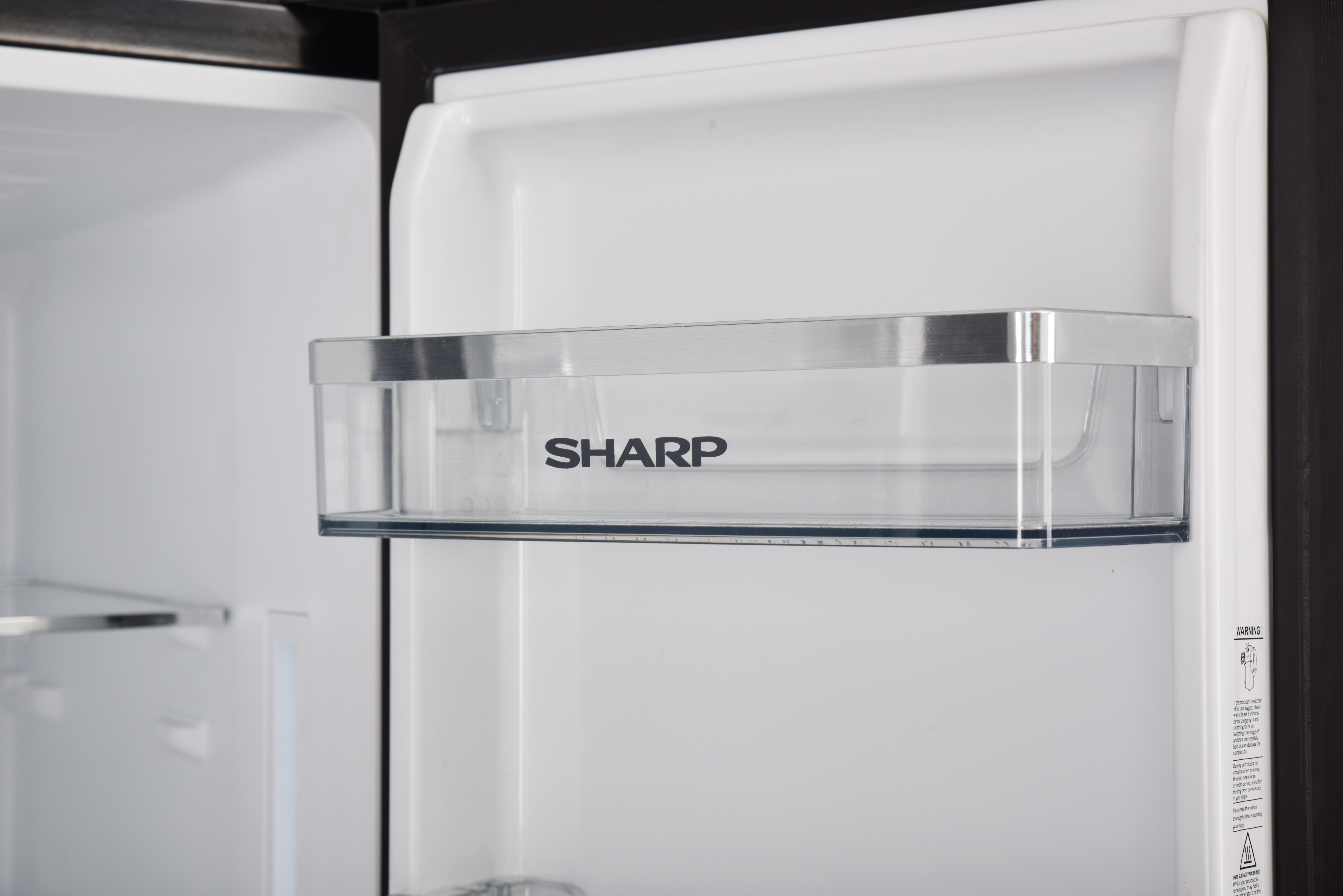 Un cassetto trasparente per frigorifero con logo SHARP e accenti argentati.