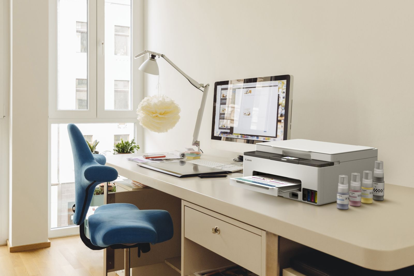 Biuro z niebieskim krzesłem, biurkiem, drukarką, komputerem i butelkami z tuszem.