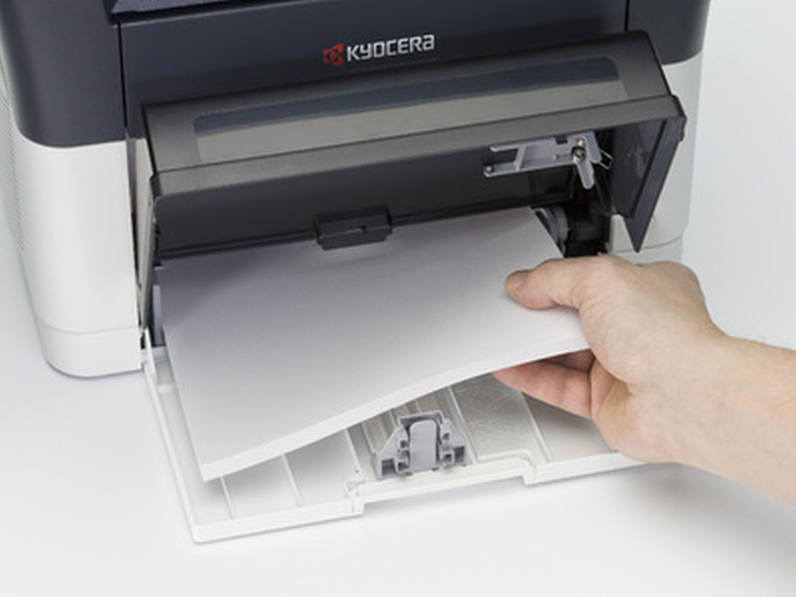 Dłoń wkłada papier do podajnika drukarki Kyocera.