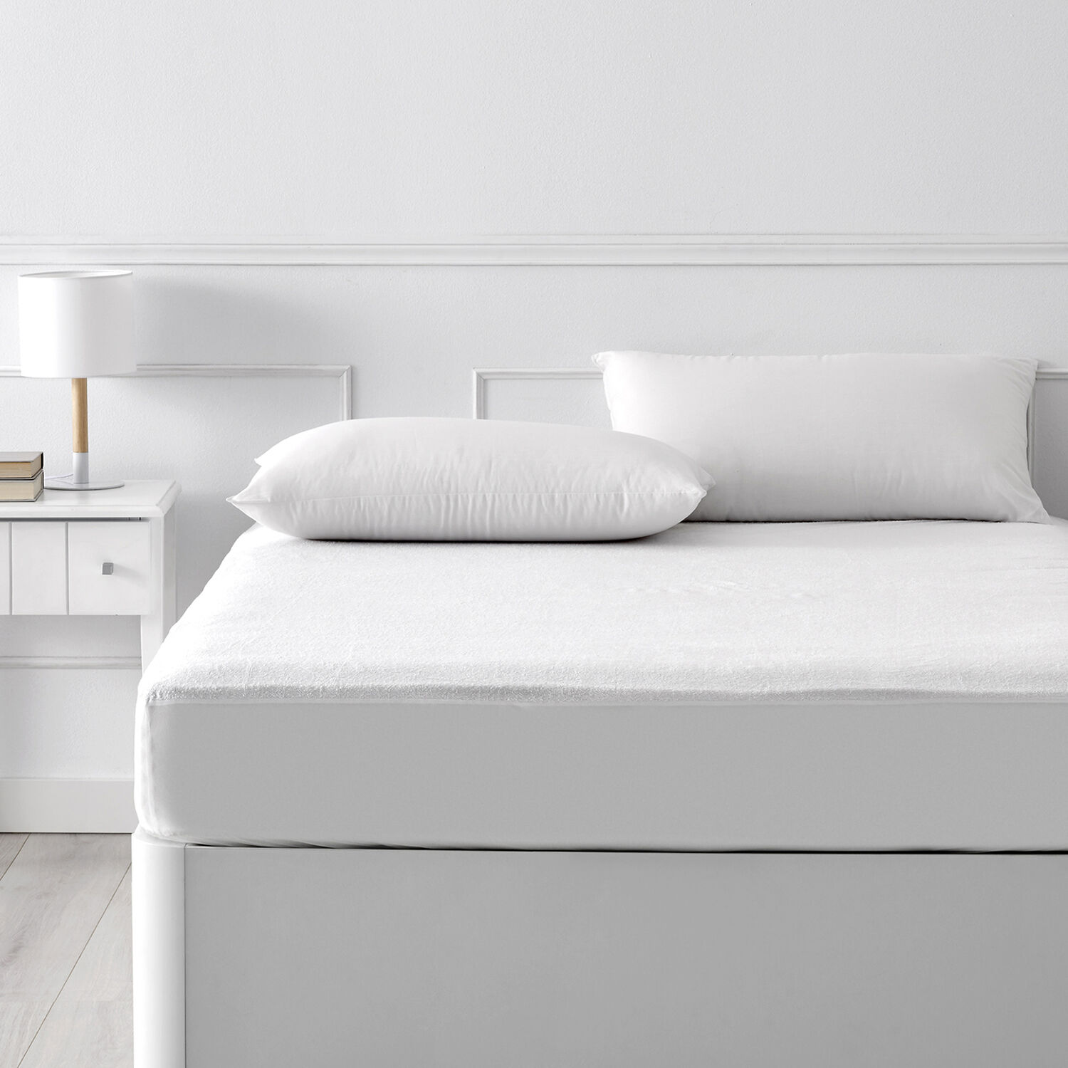 Una cama blanca con dos almohadas y una mesita de noche con lámpara.