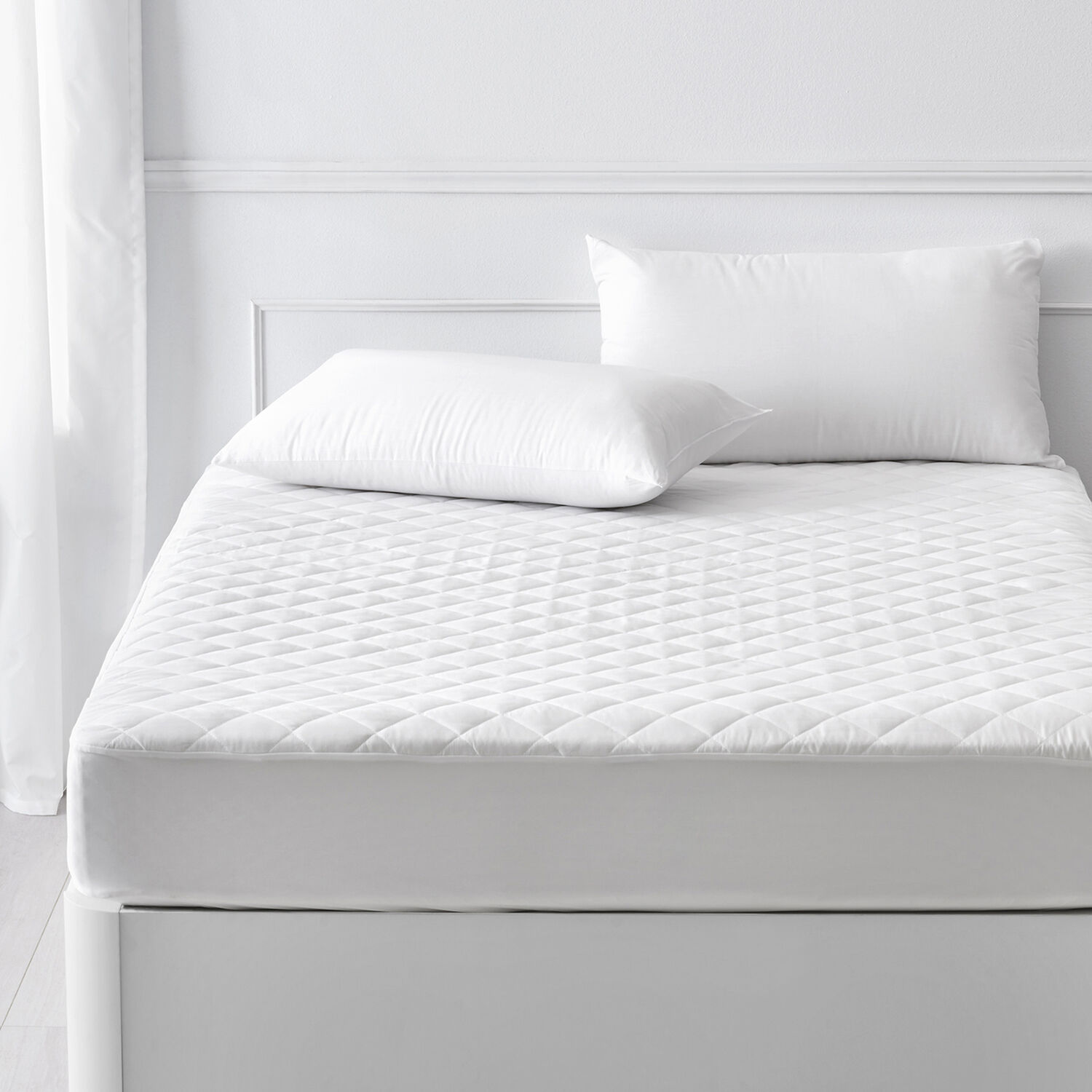 Un protector de colchón blanco acolchado con dos almohadas en una cama.