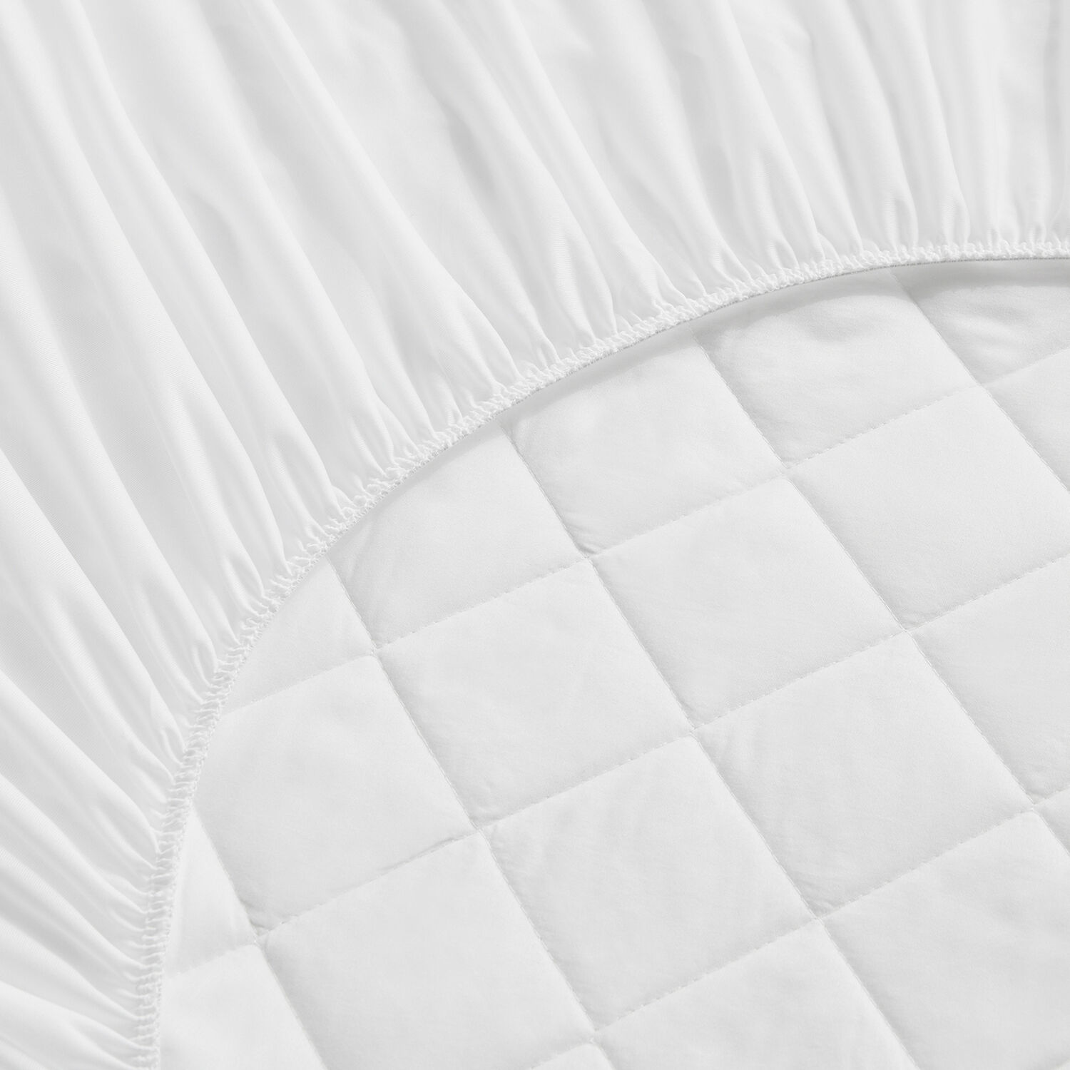 Primer plano de una sábana bajera blanca con borde elástico, que muestra textura acolchada debajo.
