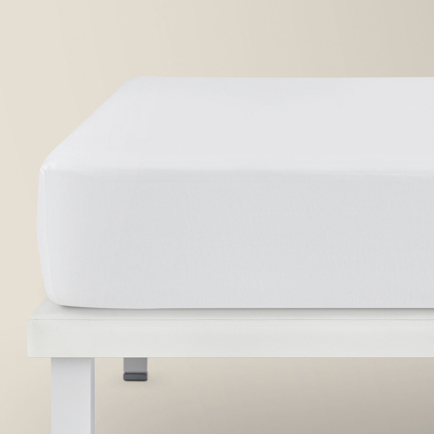 Una sábana bajera blanca sobre un somier blanco contra un fondo beige claro.