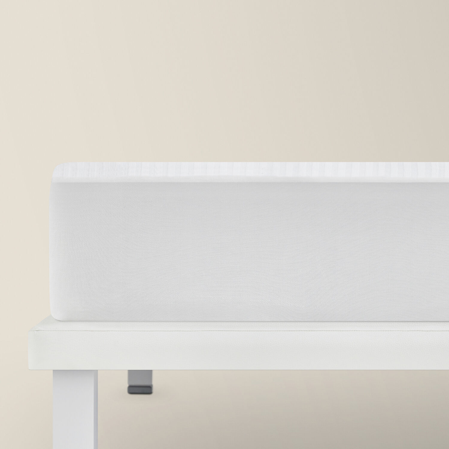 Un colchón blanco sobre una base de cama blanca contra una pared color crema.