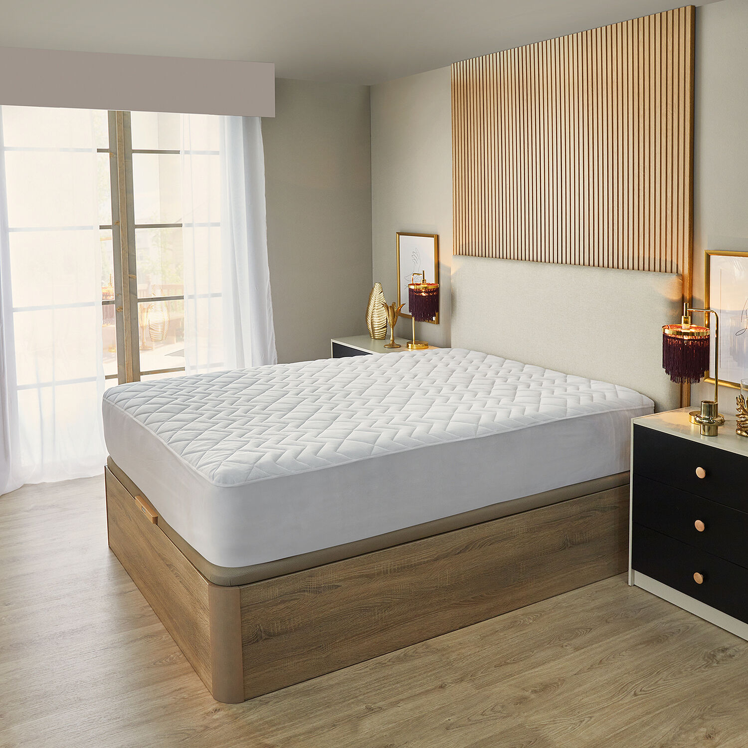 Una cama con protector de colchón blanco acolchado y base de madera, junto a una ventana.