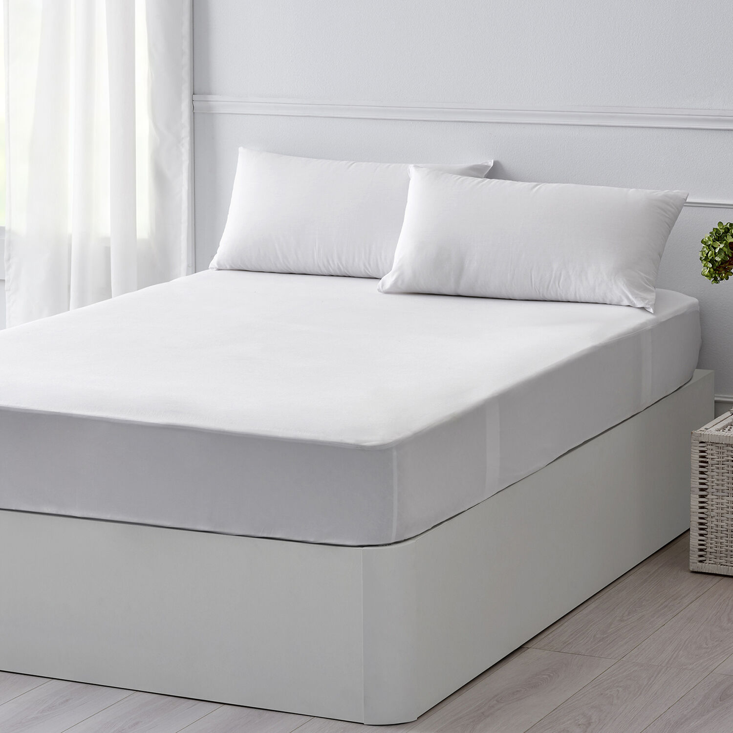 Una cama blanca con dos almohadas, cubierta con una sábana bajera blanca.