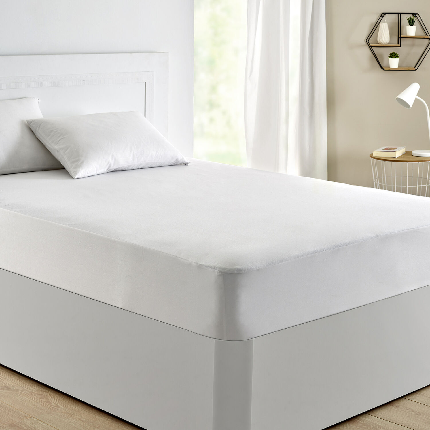Una cama blanca con almohadas y una cubierta, junto a una mesita de noche.