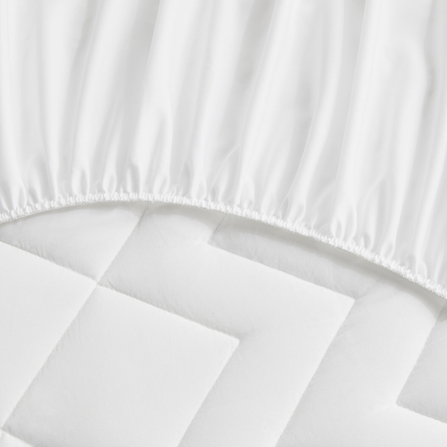 Sábana bajera blanca con borde elástico sobre protector de colchón acolchado.