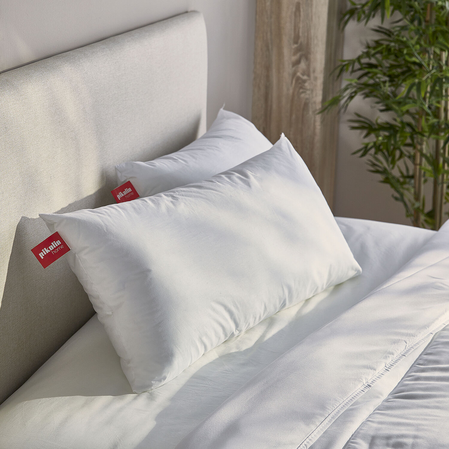 Dos almohadas blancas con etiquetas rojas descansan en una cama bien hecha.