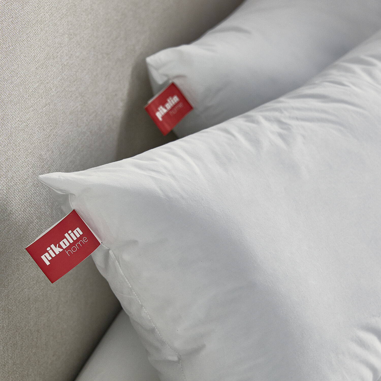 Dos almohadas blancas con etiquetas rojas de Piktolin Home sobre una cama gris claro.