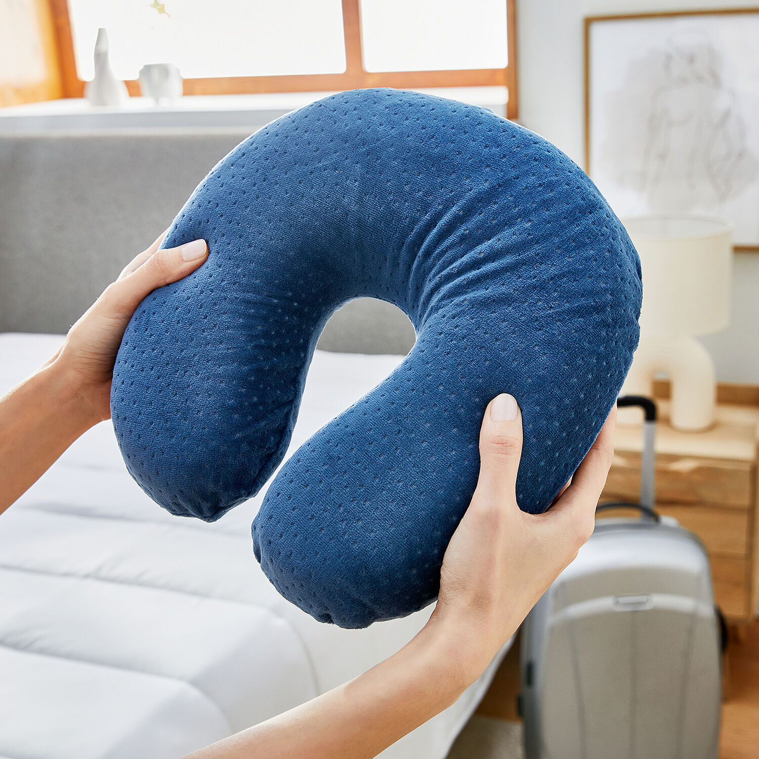 Una almohada azul con puntos se sujeta con las manos, con una maleta cerca.