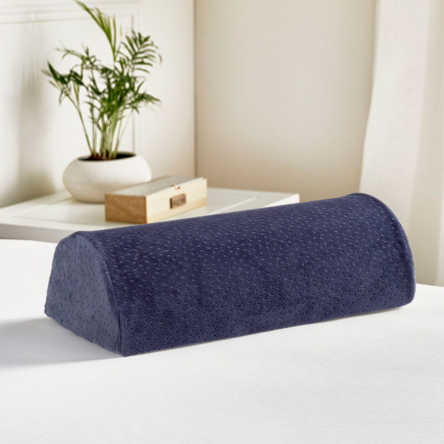 Una almohada de cuña azul oscuro con textura de puntos yace sobre una cama blanca.