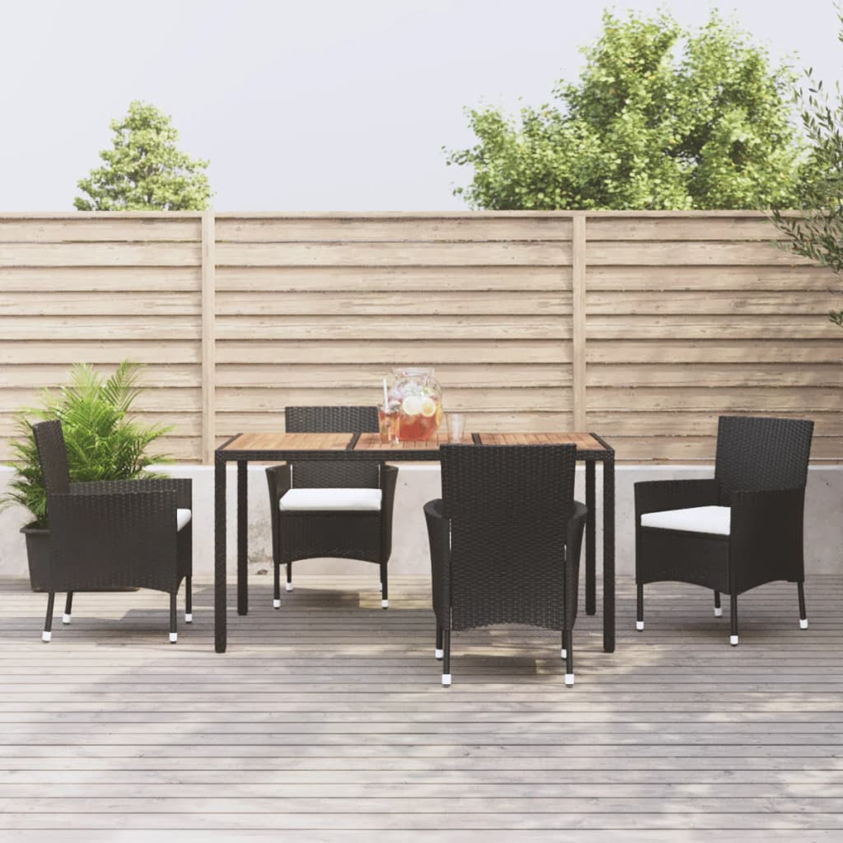 Ein Esstisch mit vier schwarzen Stühlen mit weißen Kissen auf einer Holzterrasse.