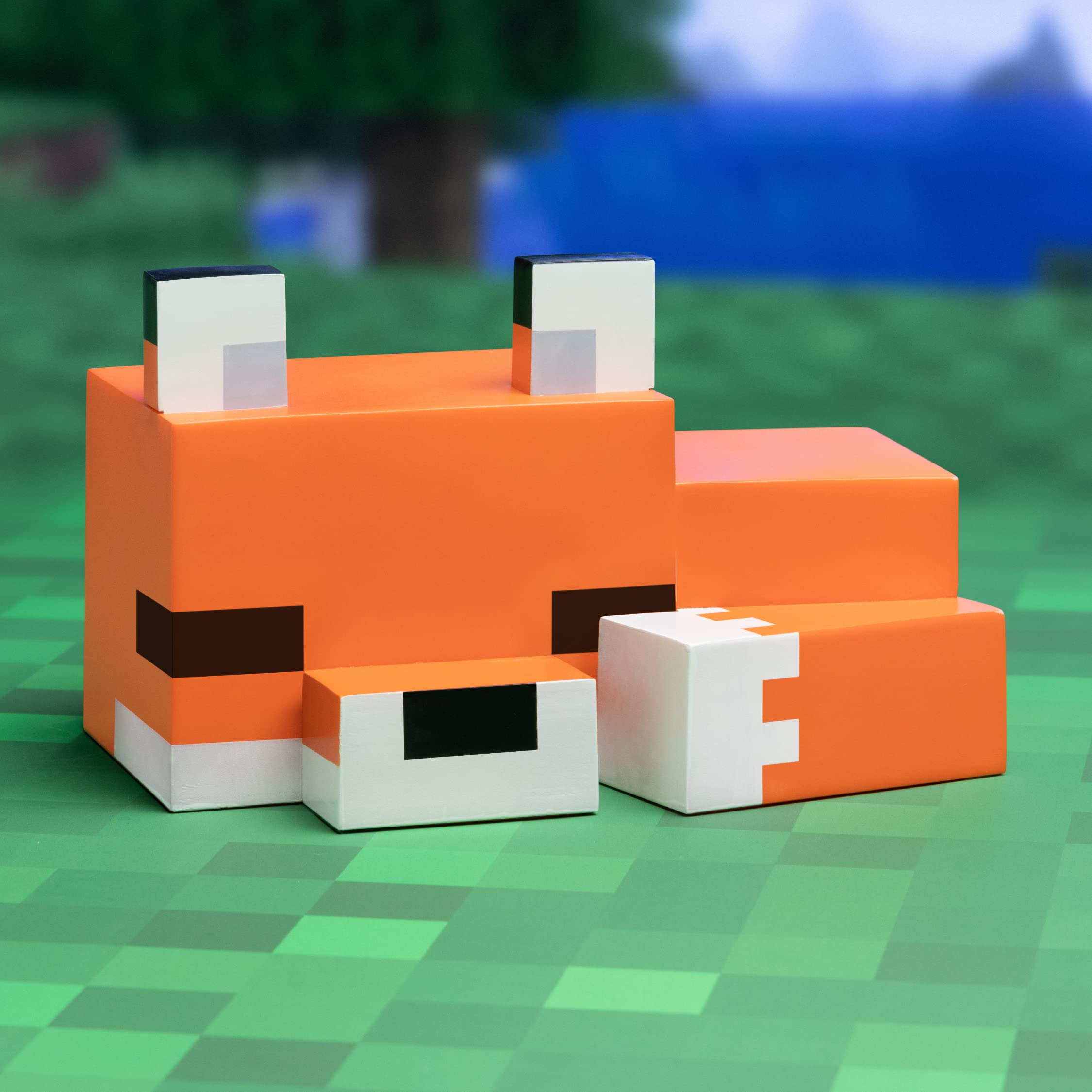 Ein orangefarbener Fuchs aus Minecraft steht auf grünem Boden mit unscharfem Hintergrund.
