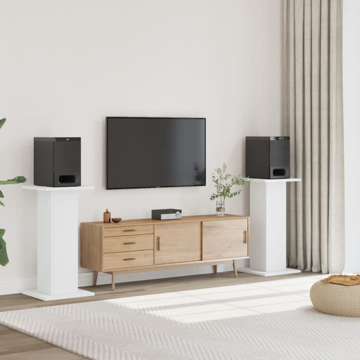 Modernes Wohnzimmer mit Fernseher, Holzschrank und zwei schwarzen Lautsprechern auf weißen Ständern.