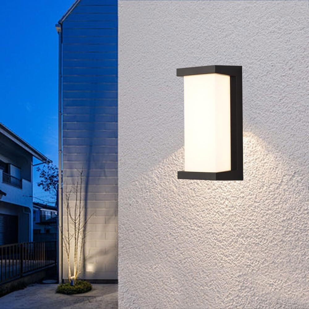 Eine weiße Wandleuchte beleuchtet eine weiße Hauswand bei Nacht.