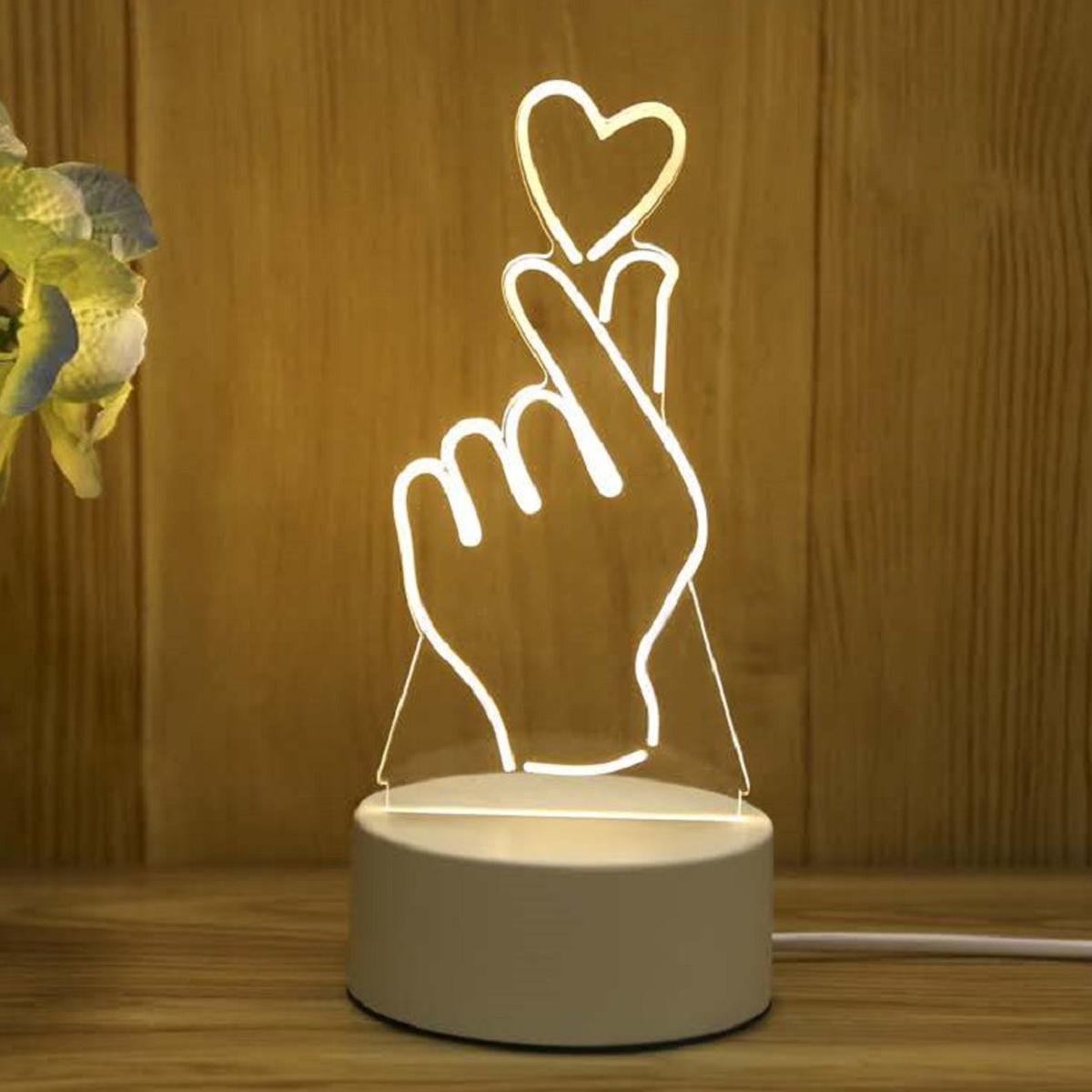 Eine Lampe in Form einer Hand, die ein Herz mit Fingern formt, leuchtet weiß.