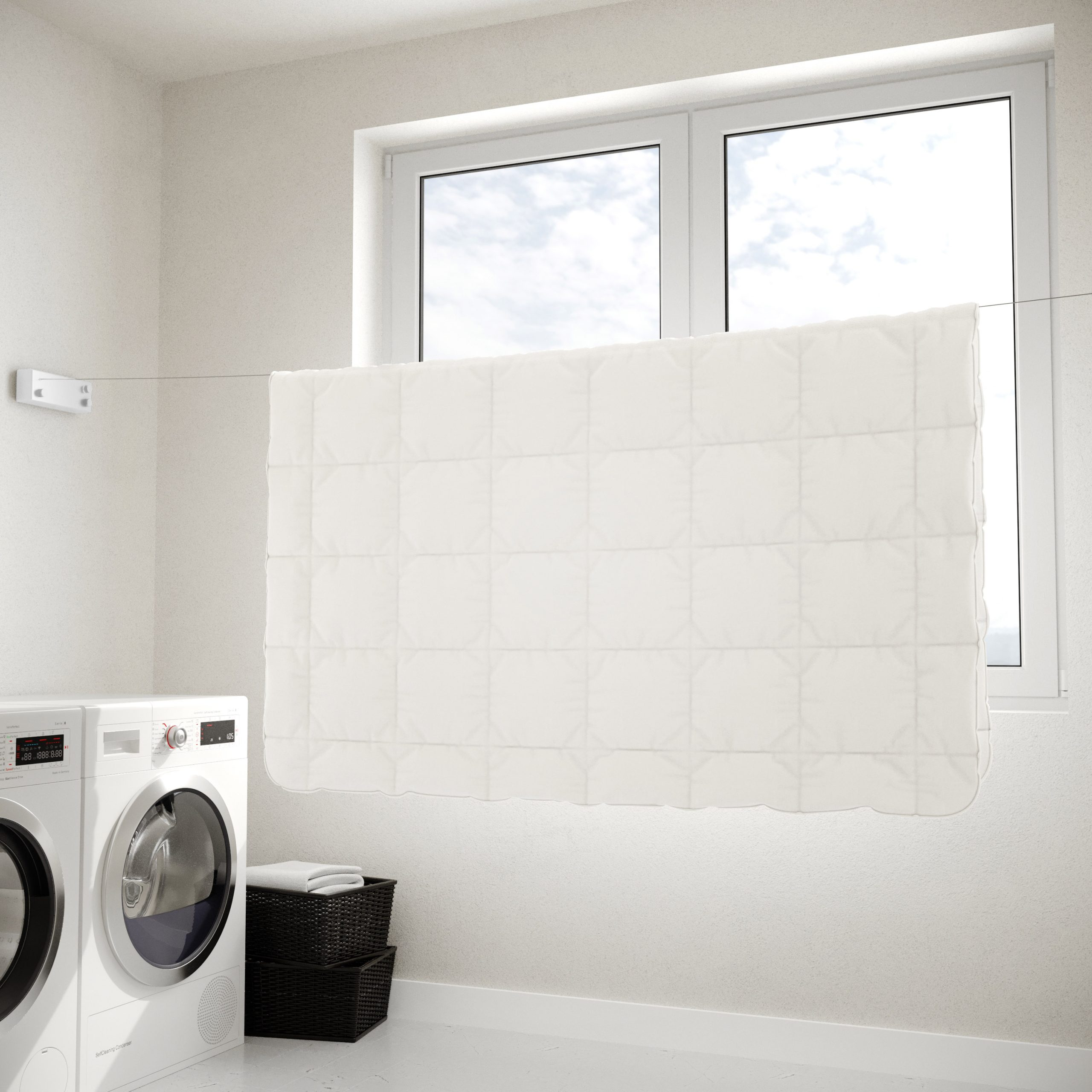 Une couette blanche est suspendue sur un fil à linge devant une fenêtre. Des machines à laver sont à proximité.