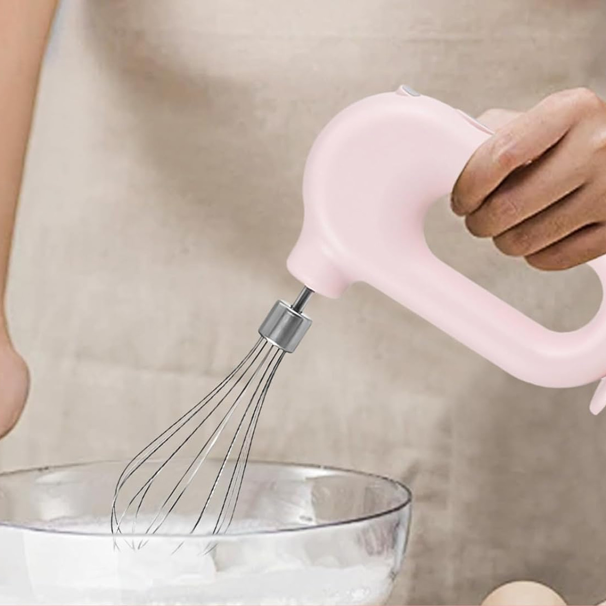 Eine Person hält einen rosa Handmixer über eine Glasschüssel mit weißem Pulver.