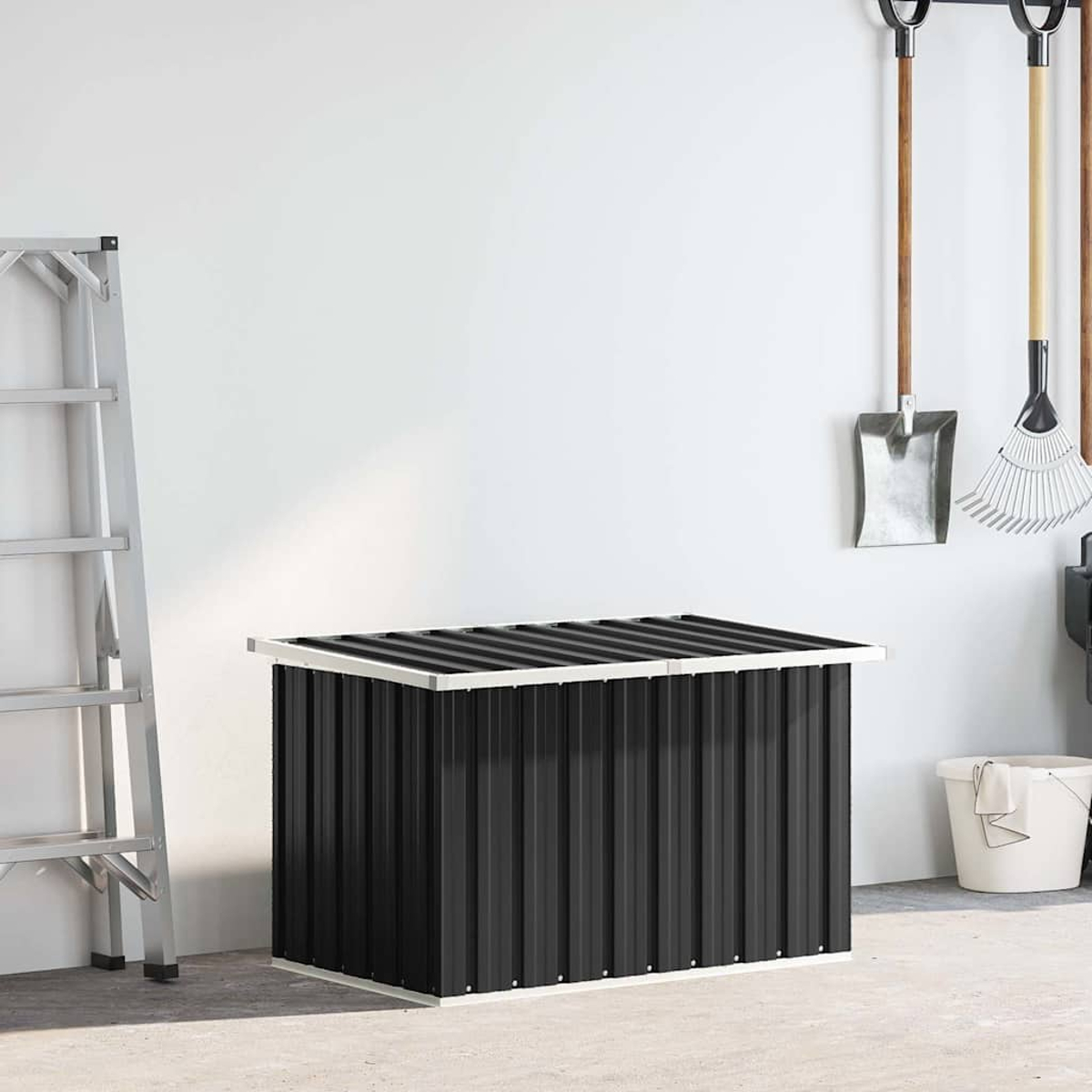 Un baule portaoggetti nero con lati scanalati in un garage. Scala a sinistra, attrezzi e secchio a destra.