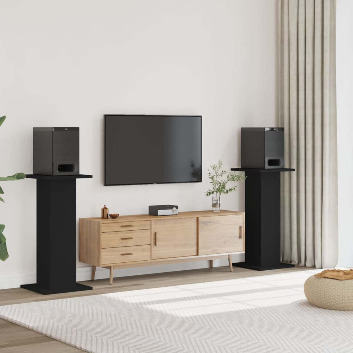Schwarze Lautsprecher auf Ständern neben einem TV über einem Holzschrank.