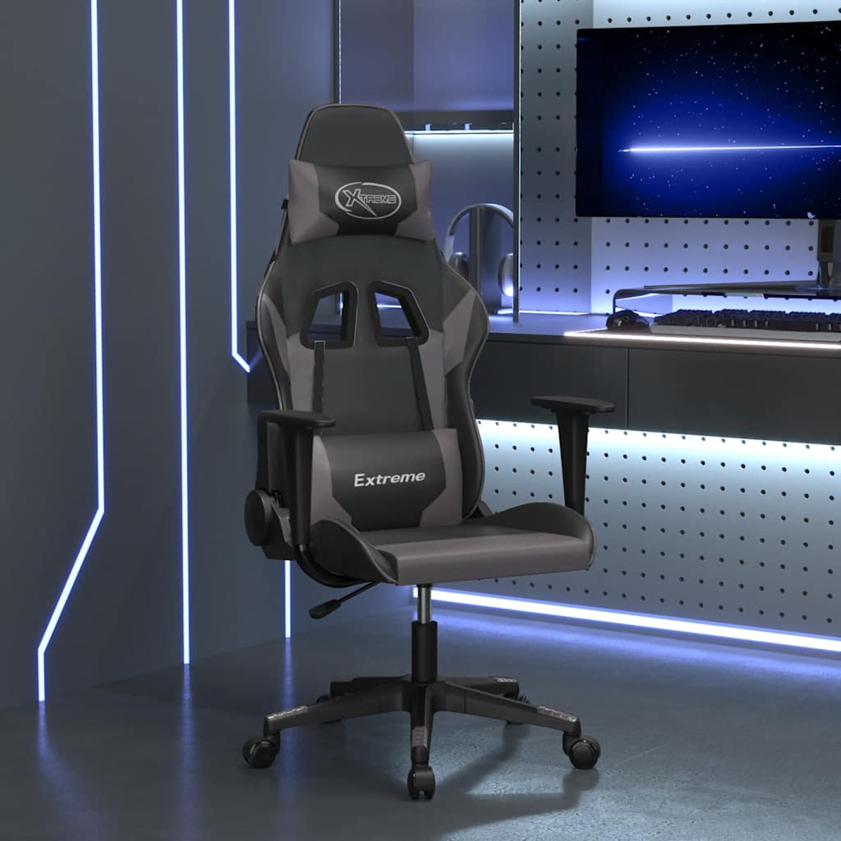 Schwarzer und grauer Gaming-Stuhl mit Kopfkissen, steht vor einem Schreibtisch mit Monitor.