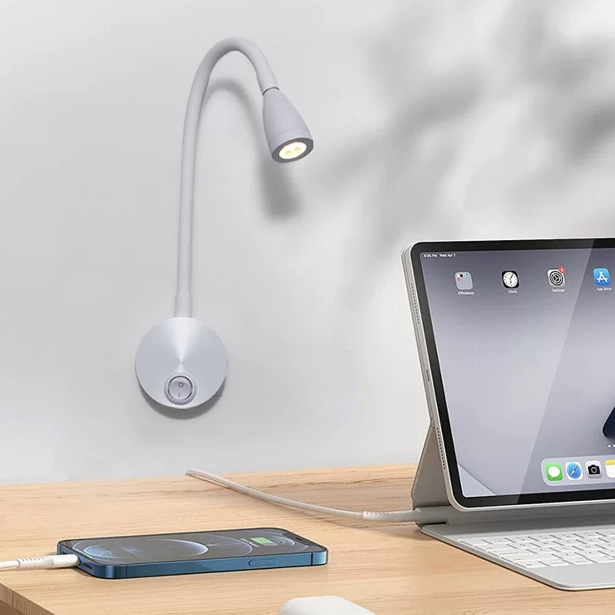 Eine weiße Nachttischlampe mit flexiblen Arm leuchtet auf ein Telefon und Tablet.