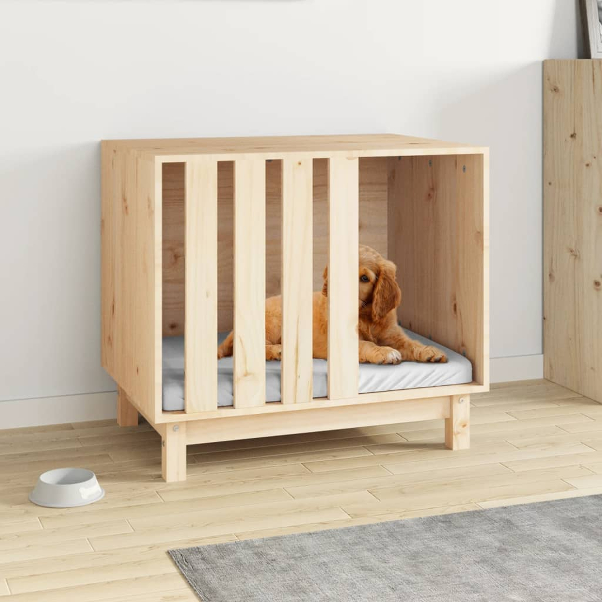 Ein Hund liegt in einem Holzkäfig auf einer grauen Matte. Ein Napf steht daneben.