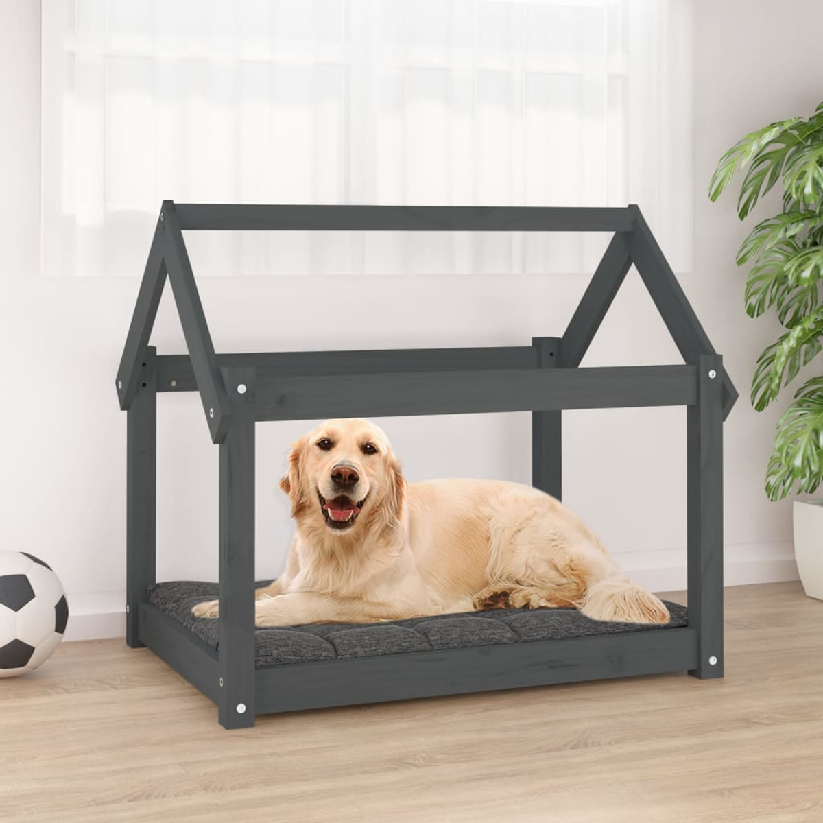 Ein Hund liegt auf einem grauen Hundebett in Hausform vor einem Fenster.
