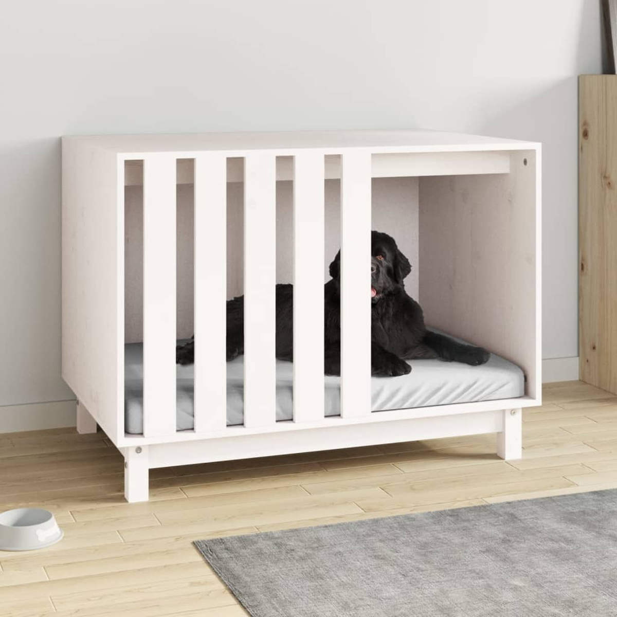 Ein schwarzer Hund liegt in einer weißen Hundebox mit einer grauen Matte.