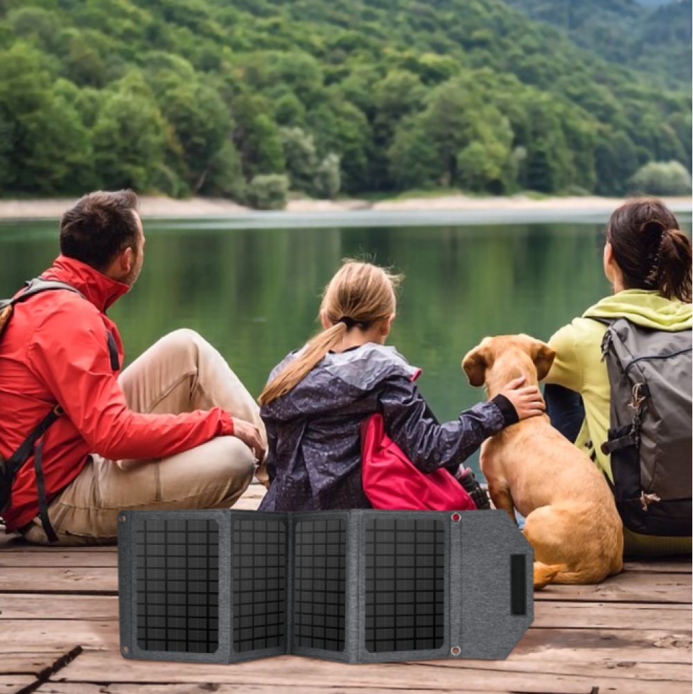 Zwei Personen und ein Hund sitzen auf einem Steg am See. Ein Solarpanel liegt im Vordergrund.