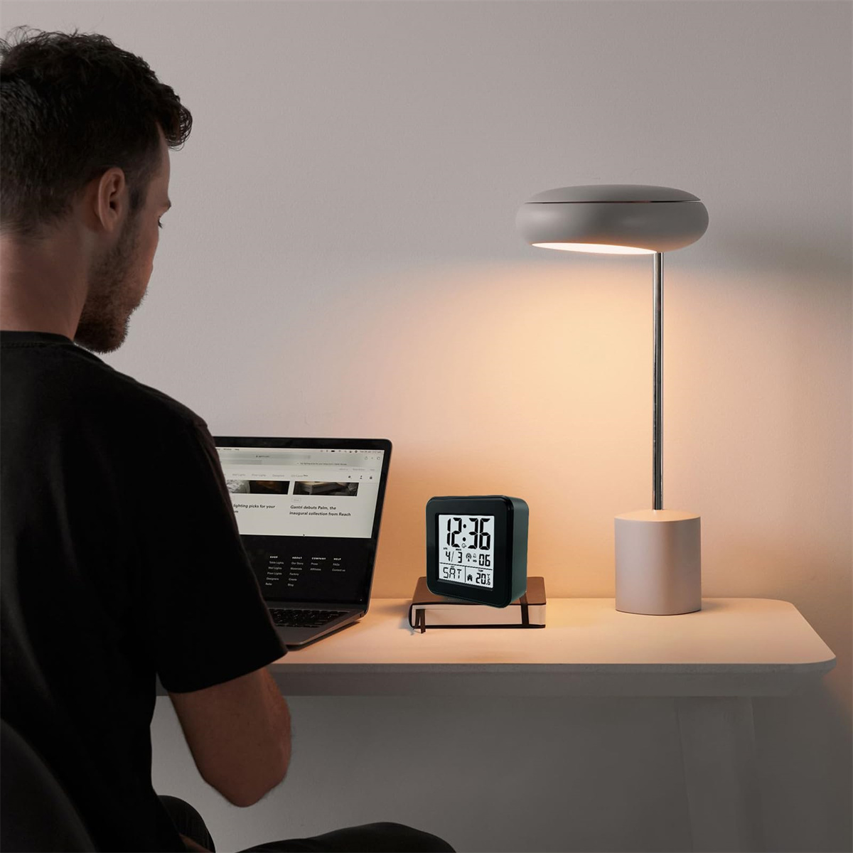 Ein Mann mit dunklem T-Shirt sitzt an einem Schreibtisch und arbeitet an einem Laptop. Eine Lampe beleuchtet den Schreibtisch.