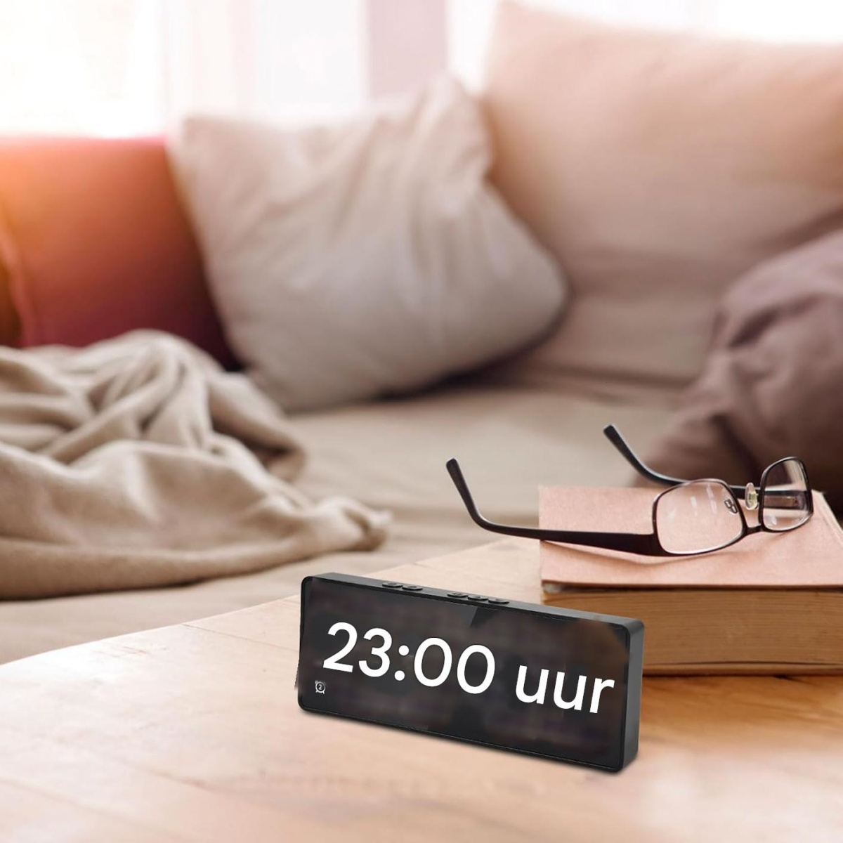 Ein digitaler Wecker zeigt 23:00 Uhr. Auf einem Buch liegen eine Brille.