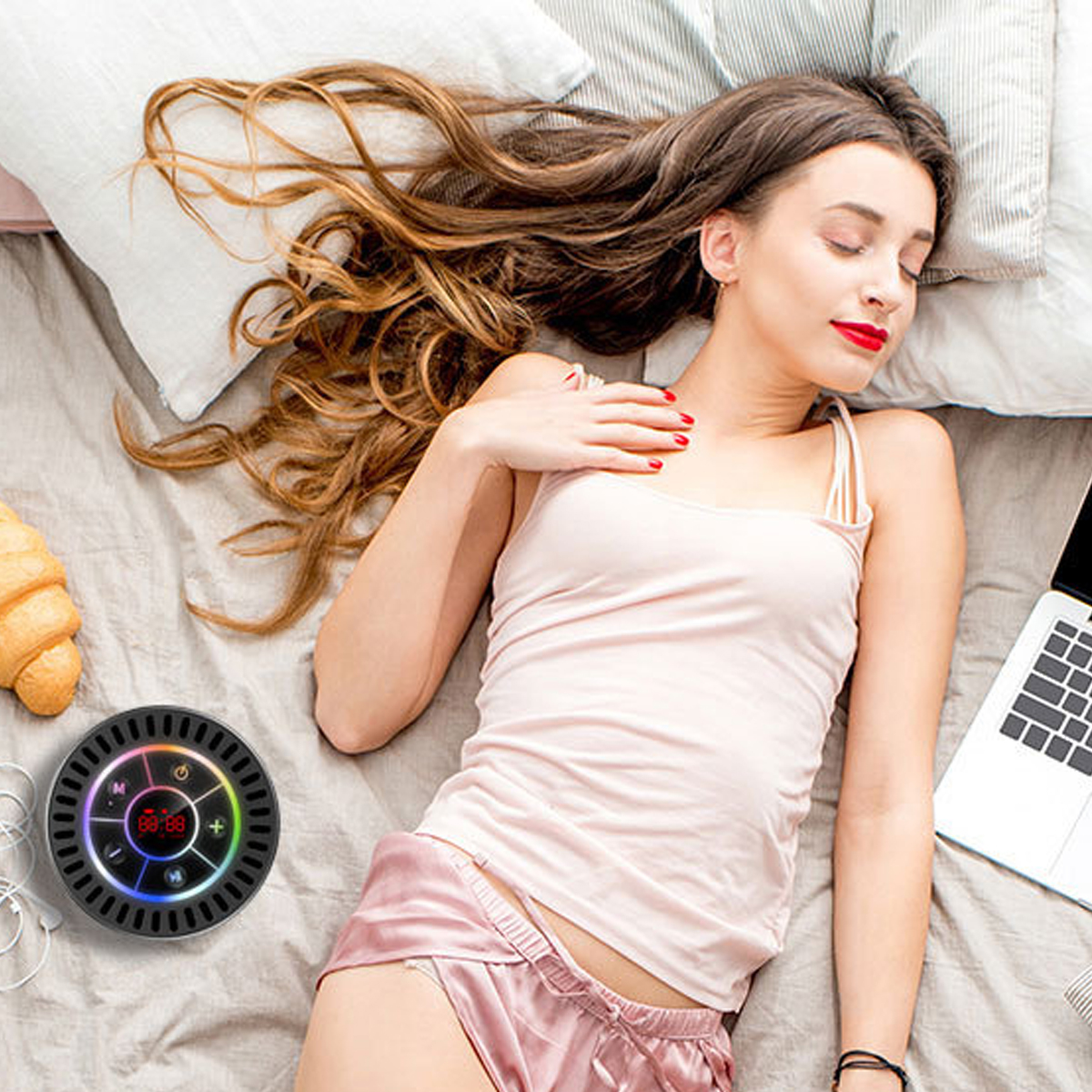 Eine Frau liegt auf dem Bett mit einem Croissant, Laptop und einem Gerät.