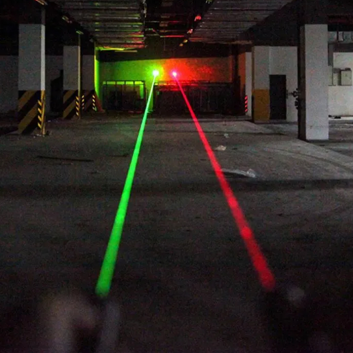 Zwei Laser, ein grüner und ein roter, projizieren Strahlen in einer dunklen, leeren Parkgarage.