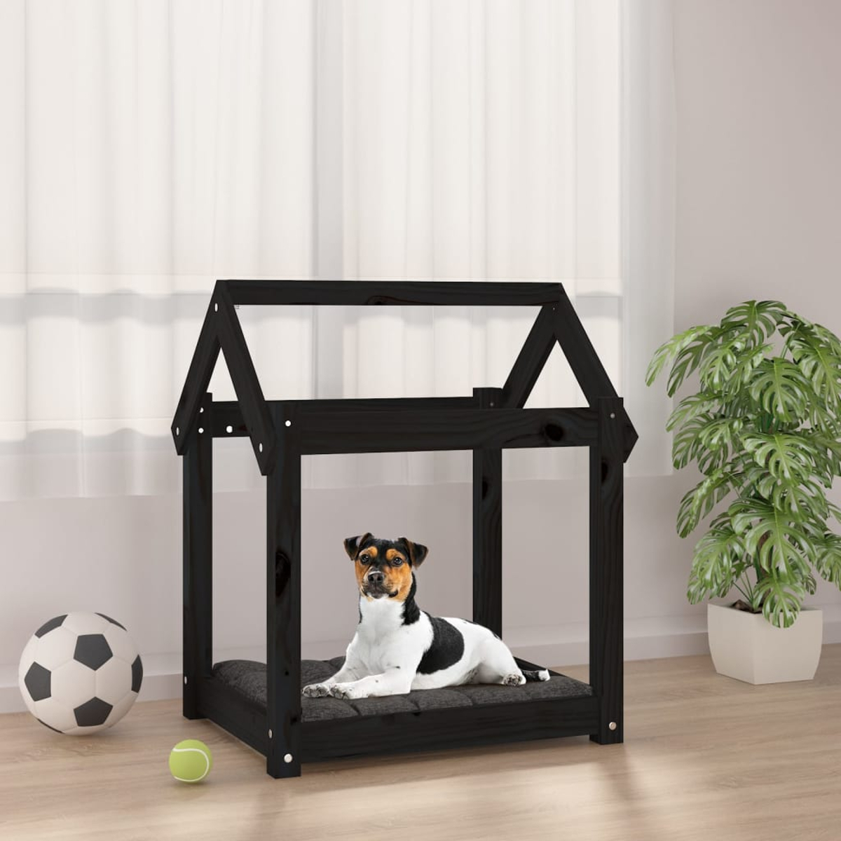 Ein schwarzer Hund ruht in einem schwarzen Hundehäuschen aus Holz mit Fußball und Tennisball.