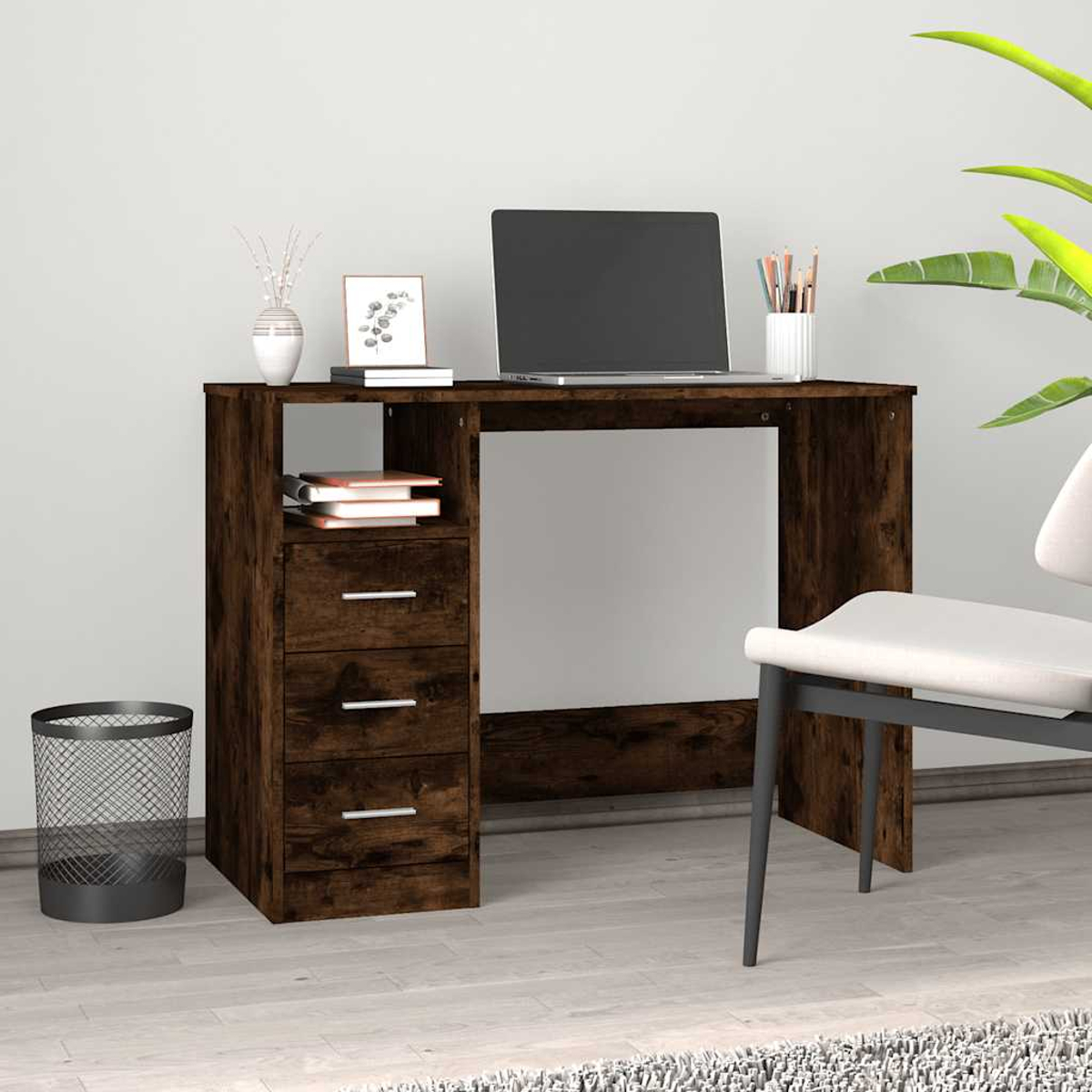 Ein dunkler Schreibtisch mit Laptop, Büchern, Stiften und einem Mülleimer.