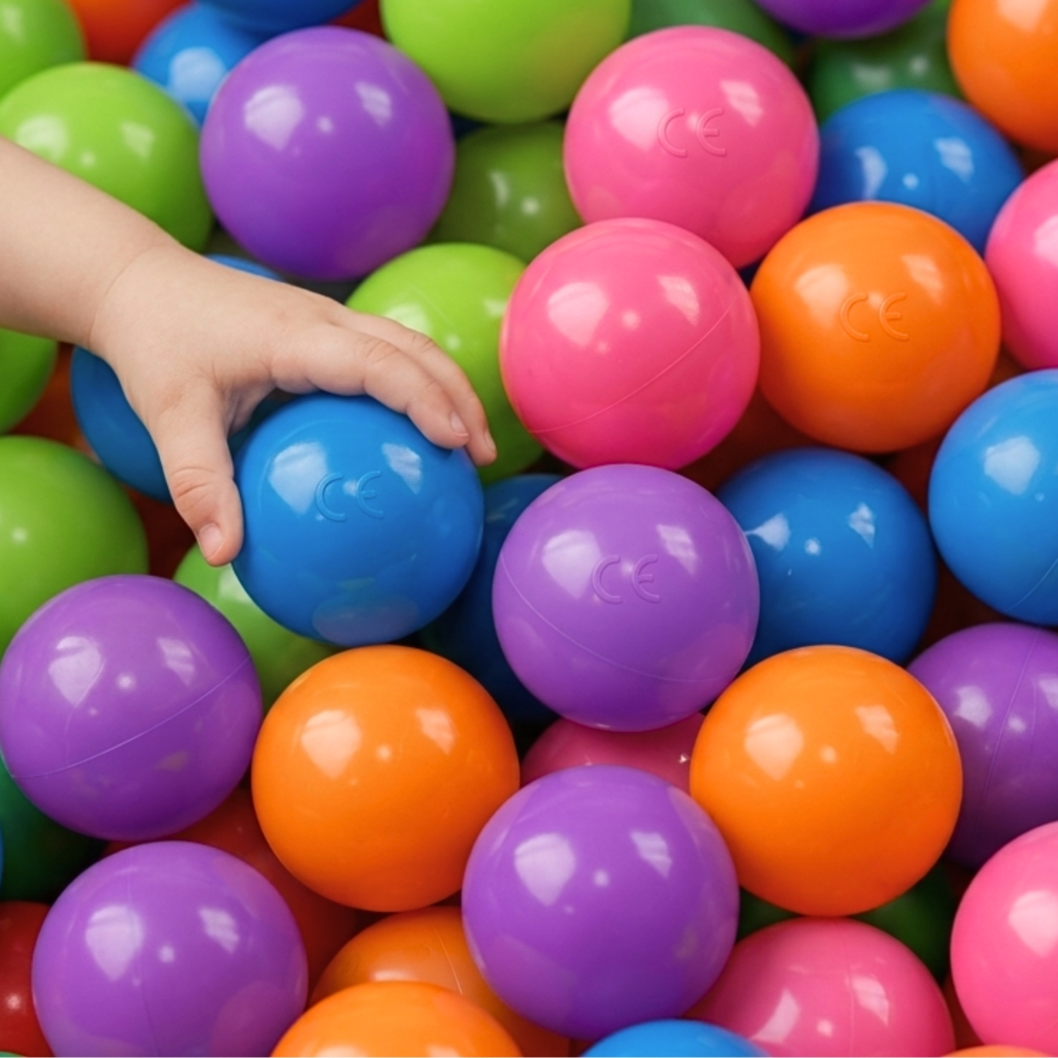 Ein Kinderarm greift nach einem blauen Ball in einem Haufen bunter Bälle.
