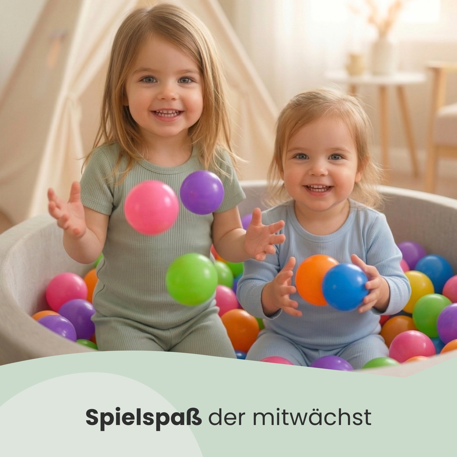 Zwei lachende Kinder sitzen in einem Bällchenbad mit bunten Bällen.