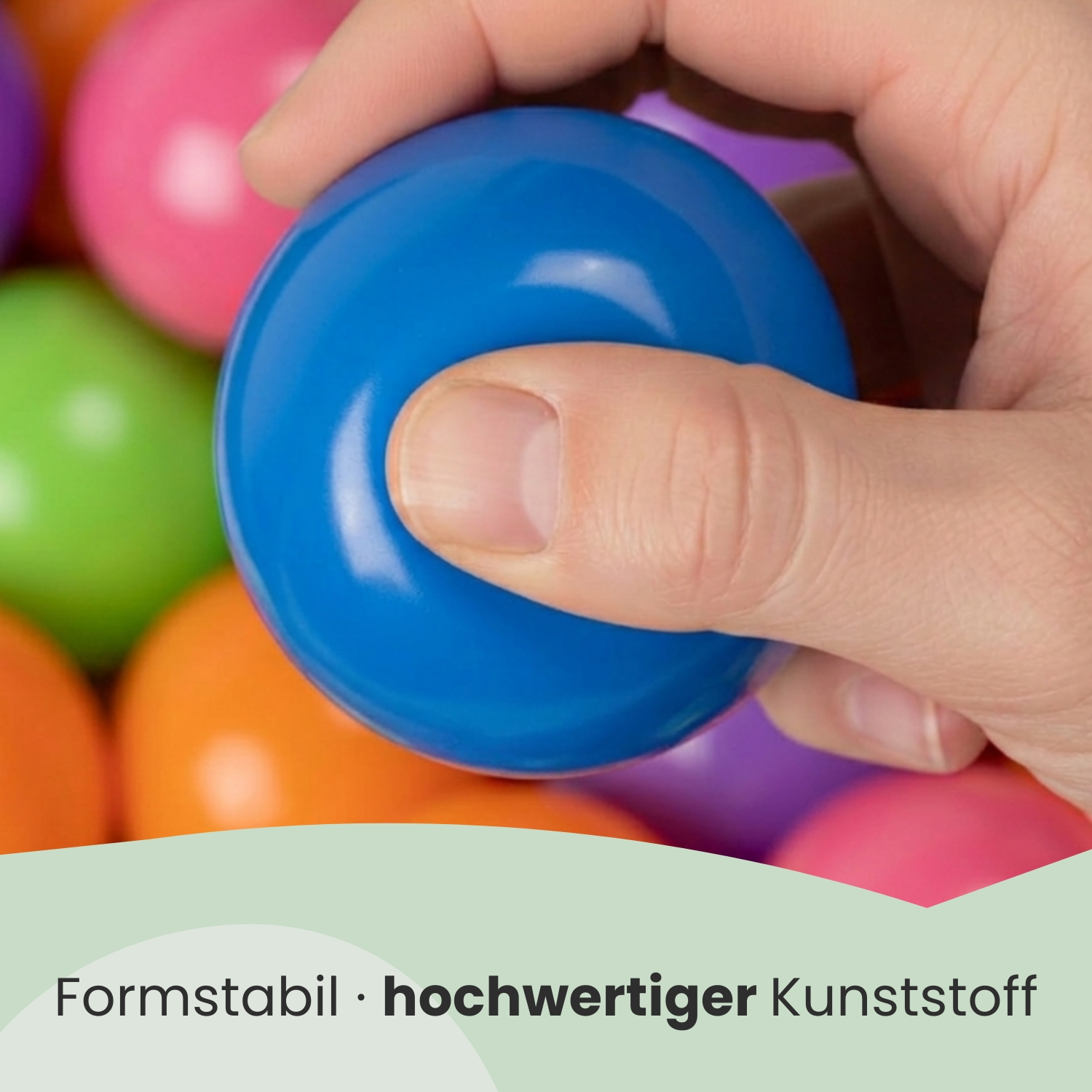 Eine Hand drückt einen blauen Ball inmitten vieler bunter Bälle.
